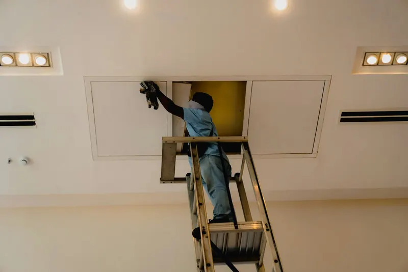 Worker on a ladder reaching into a ceiling access panel